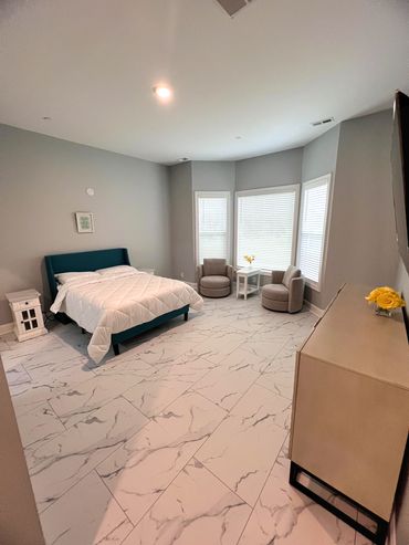 Spacious bedroom with marble floor, teal bed, and cozy seating by bay windows.