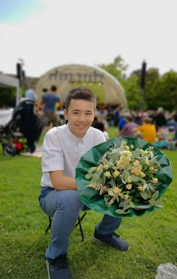 Junger Mann mit Blumenstrauß im Park bei Veranstaltung.