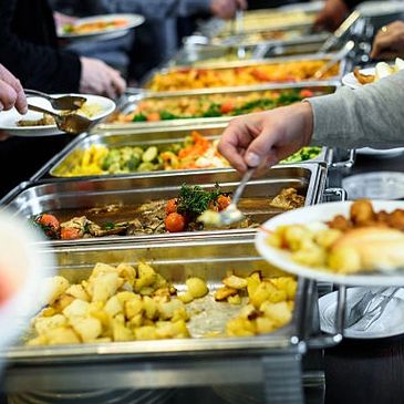 People serving themselves food from a buffet line with various dishes.