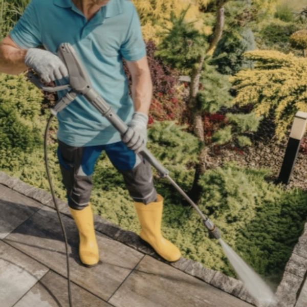 Man pressure washing outdoor tiles wearing yellow boots.