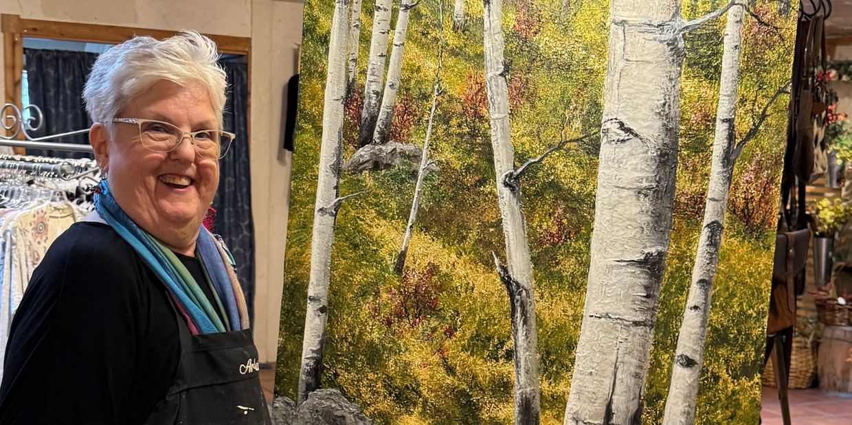 Smiling artist stands beside her detailed birch tree painting.