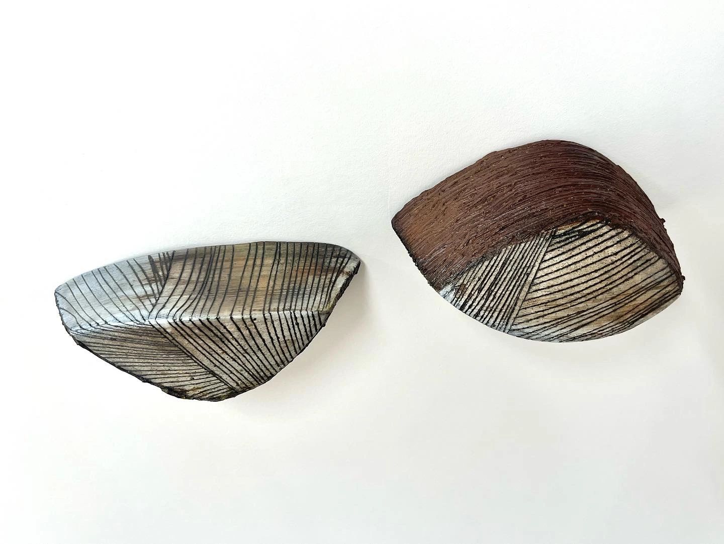 Two wall mounted pod-like ceramic sculptures, dark lines on the surface and brown texture