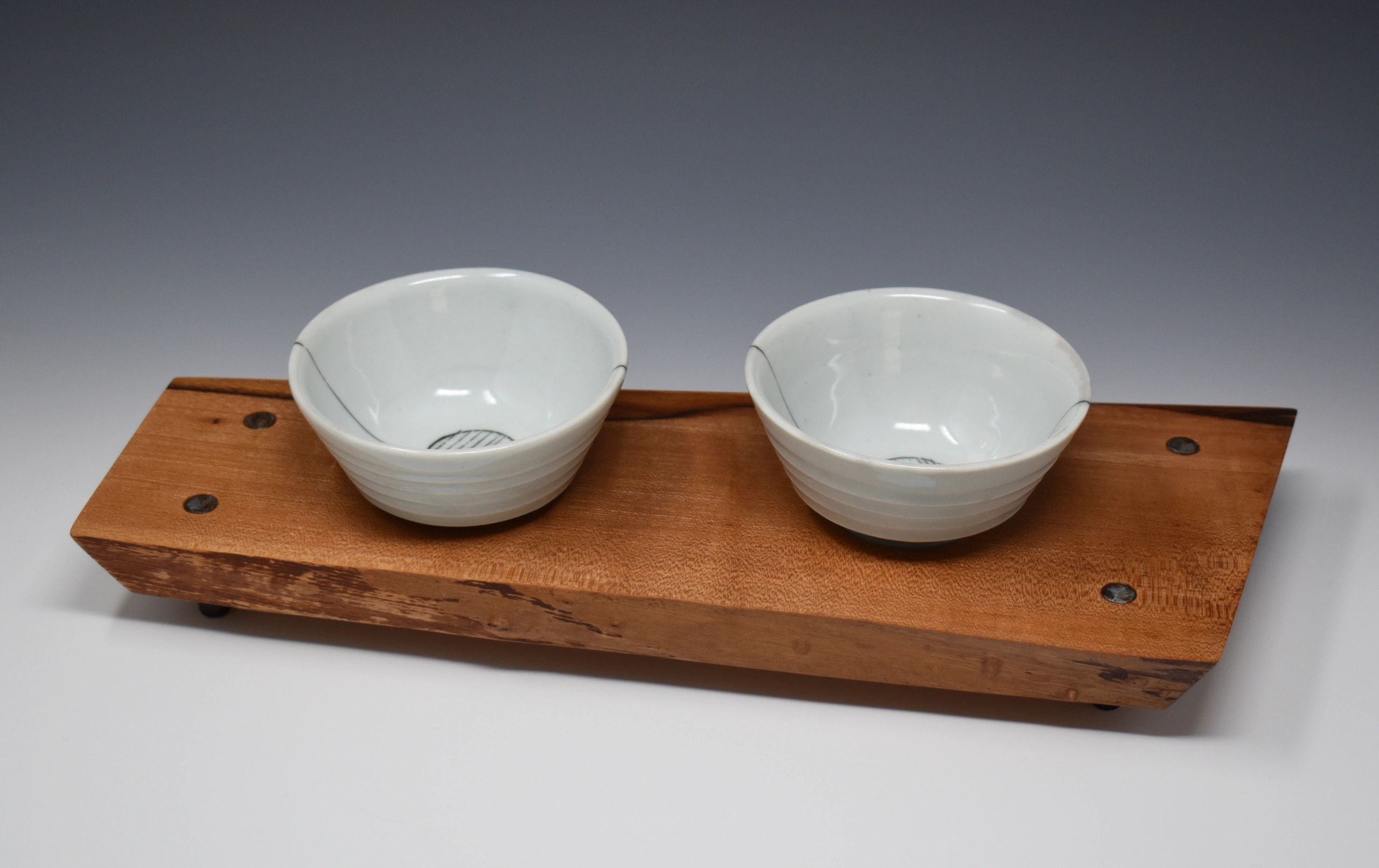 Two porcelain copitas sitting on a wood tray that has four steel legs.