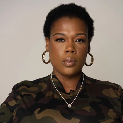 Confident woman wearing hoop earrings and camouflage top, looking directly at the camera.
