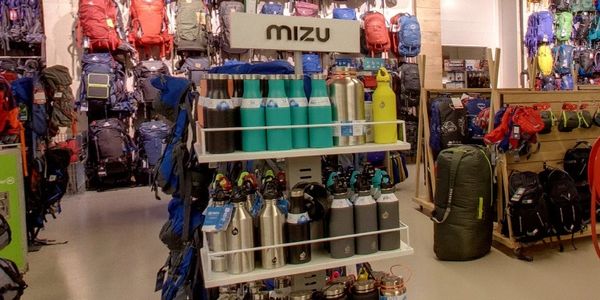 Display of Mizu water bottles surrounded by backpacks in an outdoor gear store.