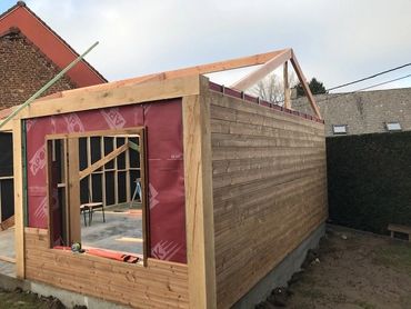 Tuinhuis in opbouw met gevelbekleding in thermo den en zicht op raamopening en dakstructuur.