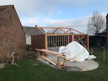 Beginfase van het tuinhuis met houten structuur op betonnen fundering, nog in ruwbouw.