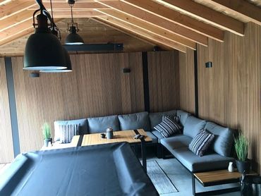 Interieur van het tuinhuis met ribbelplanken in thermo ayous, ingericht als gezellige zithoek.