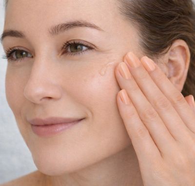 Woman applying skincare cream on her cheek with a gentle smile.
