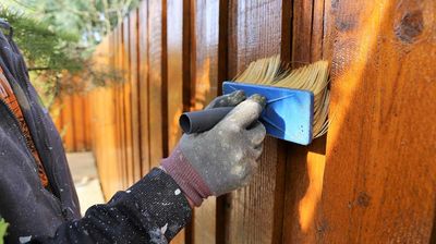 A person staining a fence with a paint bruch 