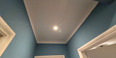 Ceiling light fixture illuminating a blue-walled hallway with white door frames.