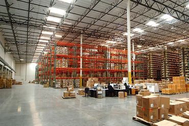 A spacious warehouse filled with tall shelving units stacked with boxes, and office workers