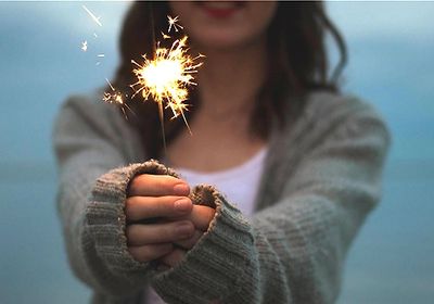 female smiling holding a lit sparkler out in front of her. Counseling support therapy encouragement