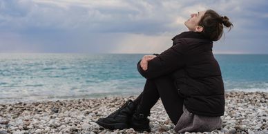 Woman sitting on a rocky beach looking relaxed. Dalena Watson Counseling meditation videos, youtube