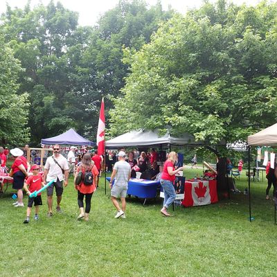 People enjoying a Canadian outdoor event with flags and tents on a sunny day.