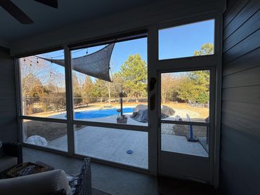 View of a backyard pool and patio from inside a screened porch.