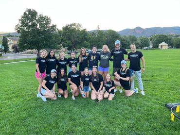 Group of people posing on a green field with mountains in the background.