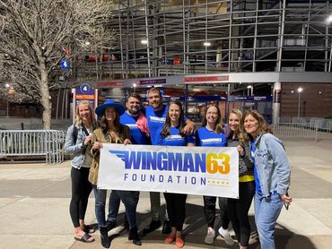 A group holding a Wingman63 Foundation banner outside a stadium at night.