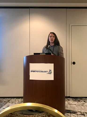 Woman speaking at a podium during a sport psychology event.