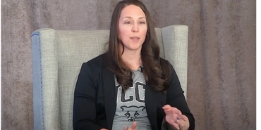 Woman in casual attire speaking while seated in a comfortable chair.