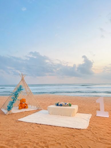 Beach setup with teddy bear, flowers, and number one.