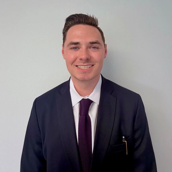 Smiling man in a suit and tie against a plain background.