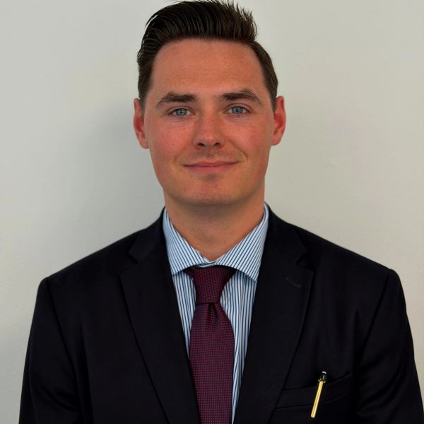 Man in a suit with a maroon tie and a pen in his pocket.