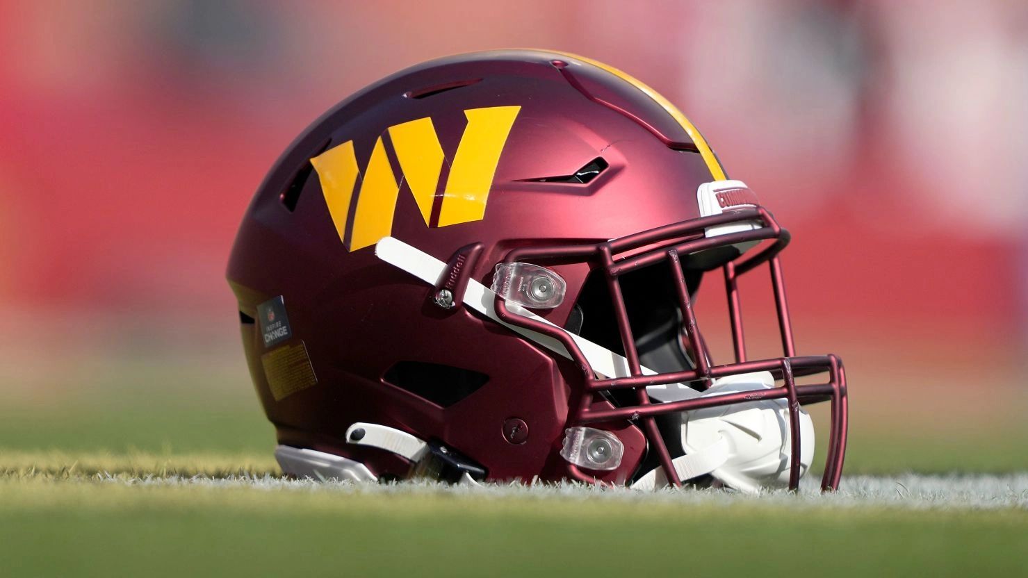 Maroon football helmet with a yellow 'W' on the side on the grass.