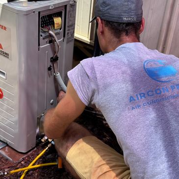 Technician repairing an outdoor air conditioning unit with tools nearby.