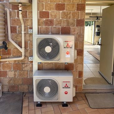 Two Mitsubishi air conditioning units mounted on a brick wall outside a door.
