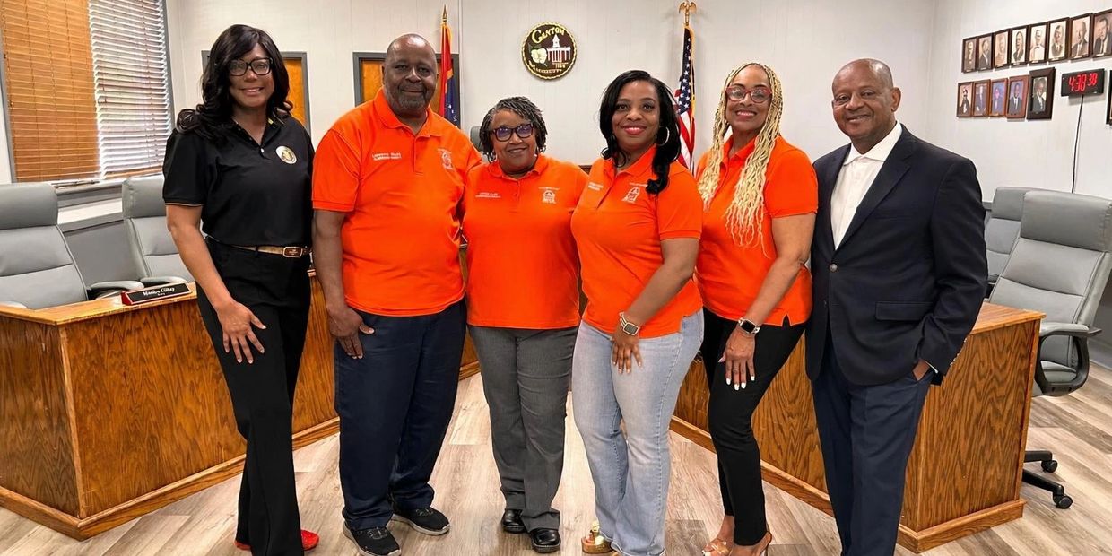 Six professionals posing together in a formal office setting, with four wearing orange shirts.