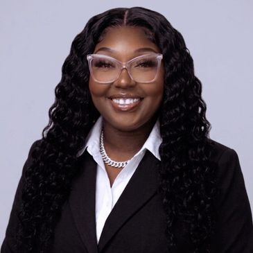Professional woman in a black suit with curly hair and glasses smiling.