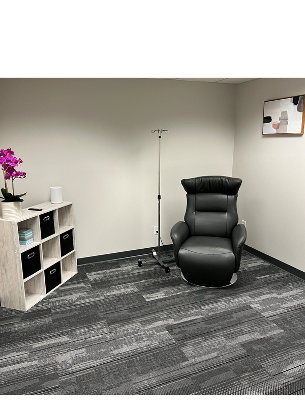 Clean, well-lit ketamine treatment room; a black leather recliner, pink orchid on a white table.
