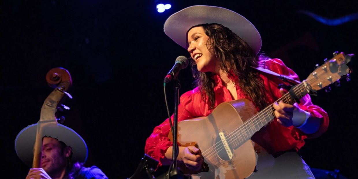 Woman singing and playing guitar on stage wearing a cowboy hat.