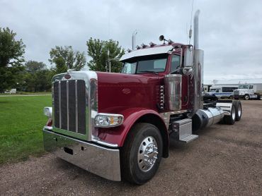 A maroon semi-truck parked on a gravel road.