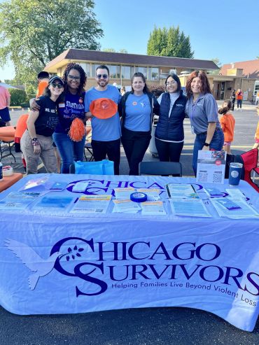 Group of volunteers at Chicago Survivors booth with informational materials outdoors.