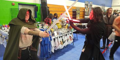 Two people in cosplay duel with a sword and a red lightsaber at a convention.