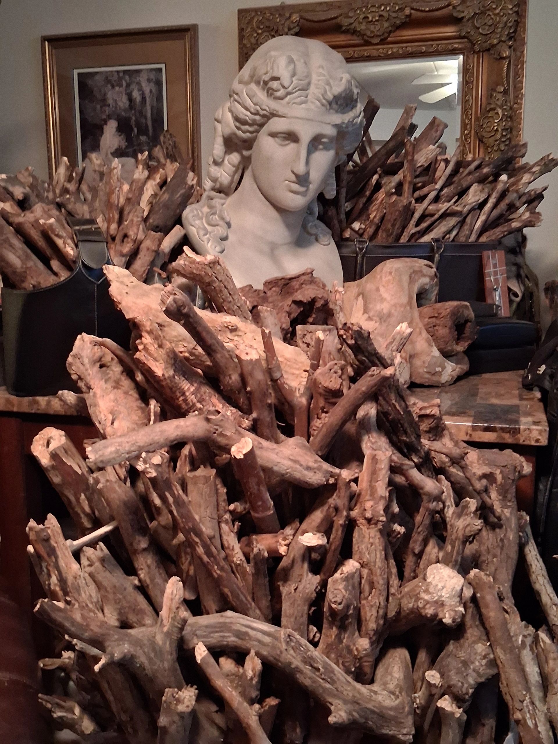 Bust sculpture behind a large pile of rustic wooden sticks indoors.