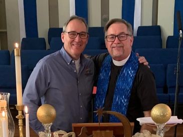 Two men smiling together in a church setting with candles.