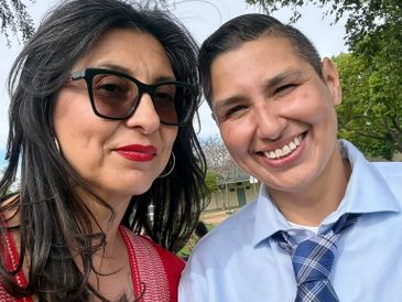 Two people smiling outdoors, one wearing sunglasses and the other in a tie.