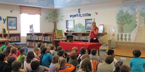 A woman reads to children in a colorful library setting.