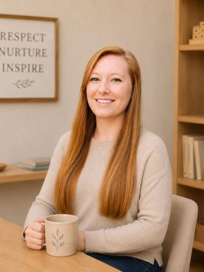 Woman with long red hair holding a coffee mug and smiling.