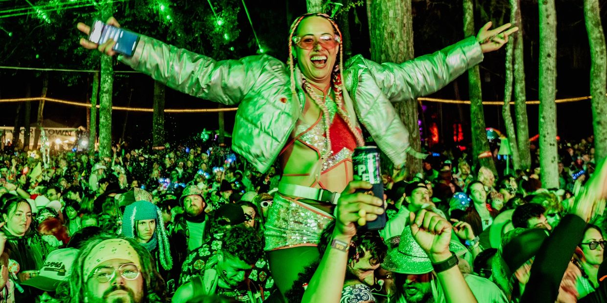 Person celebrating at a lively outdoor night event with green lighting.