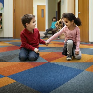 Two children holding hands and smiling while kneeling on a colorful carpet.