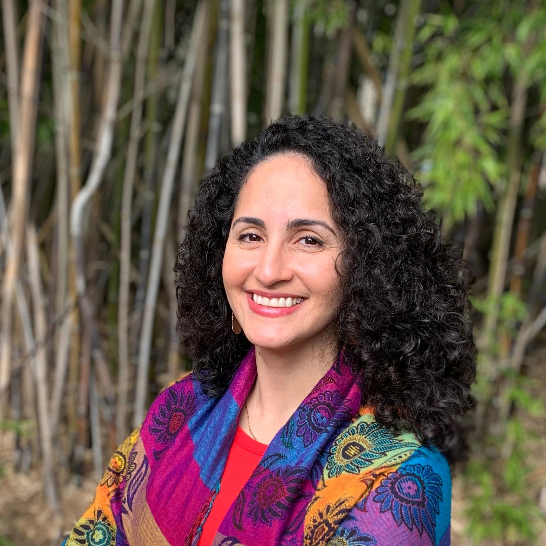 Headshot of a woman with curly hair, light brown skin color, wearing a multicolor shawl