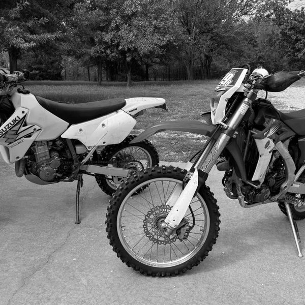 Two dirt bikes, one yellow Suzuki and one blue Yamaha, parked outside on a concrete surface.