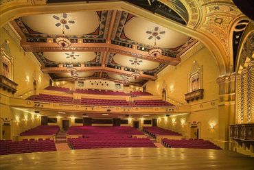 Elegant theater auditorium with ornate ceiling and red seats.