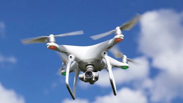 A white quadcopter drone with a camera flying against a blue sky.