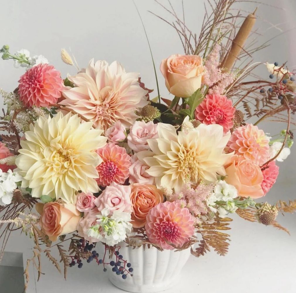 Elegant bouquet with peach, cream, and pink flowers in a white vase.