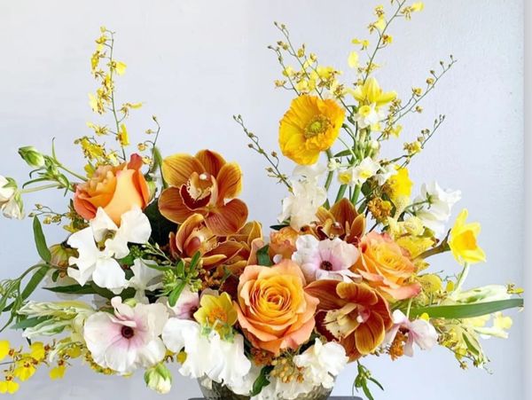 Elegant floral arrangement with yellow, orange, and white flowers in a vase on a black marble table.